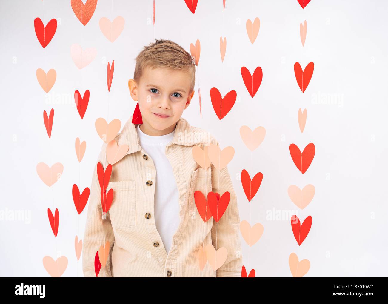 Niedliches Kinderportrait umgeben von hängenden roten Herzen auf weißem Hintergrund. Liebe, Zärtlichkeit, Kinderunschuld Stockfoto