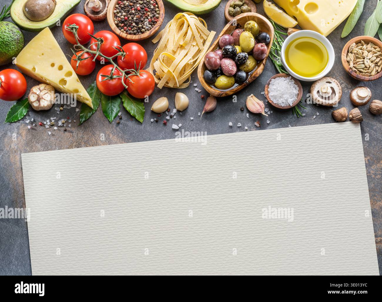 Mediterrane Zutaten wie Pasta, Olivenöl und Gemüse auf einer Steinküche mit leerem Aquarellpapier für Text oder Rezept Stockfoto