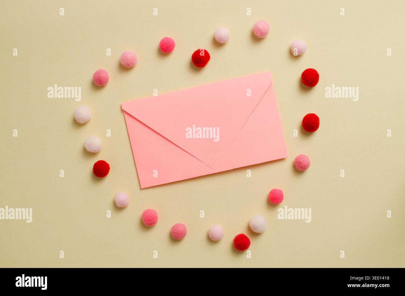 Eine pinkfarbene Postkarte auf hellgelbem Hintergrund, umgeben von einem Kreis flauschiger Pompons in Rot-, Rosa- und Weißtönen. Ein festliches romantisches c Stockfoto