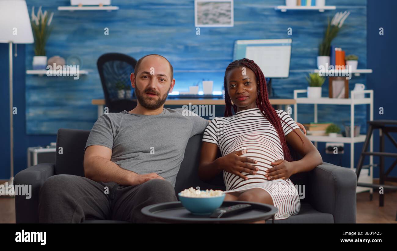 Schwanger interracial paar mit Videokonferenz für Remote-Online-Kommunikation zu Hause. Menschen mit gemischter Rasse, die ein Baby erwarten und mit Freunden mit Technologie im Wohnzimmer sprechen Stockfoto
