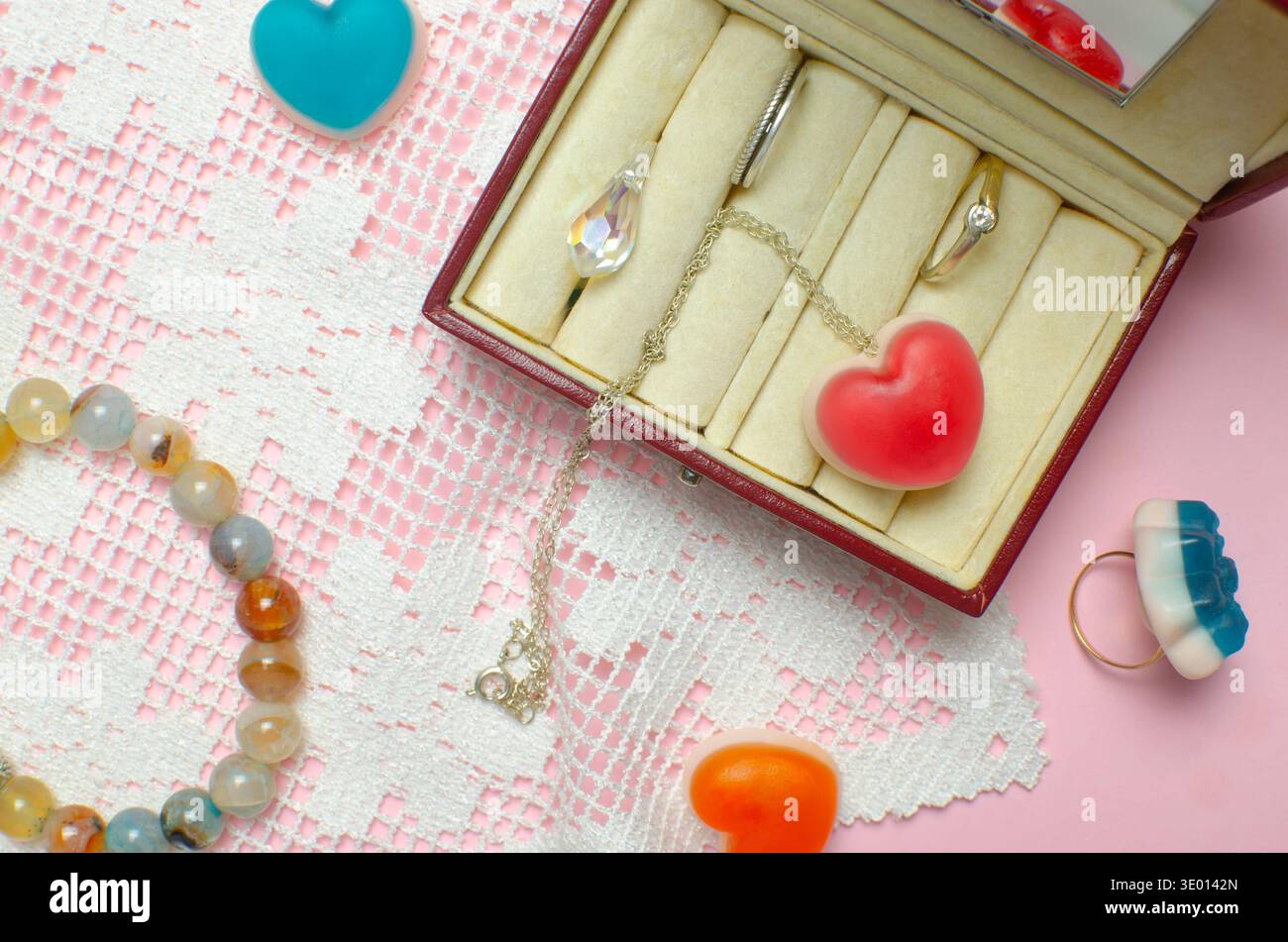 Schmuckschatulle auf rosa Hintergrund: Ringe, Halskette mit Gelee rotem Herz, Kristall und bunte Accessoires. Gelee Bonbons in Form von Herzen. Conceptu Stockfoto