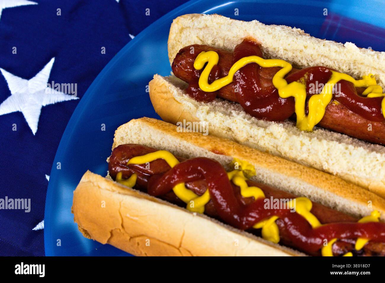 Nahaufnahme zweier klassischer amerikanischer Hotdogs mit Ketchup und Senf, präsentiert auf einer blauen Platte vor dem Hintergrund der US-Flagge Stockfoto