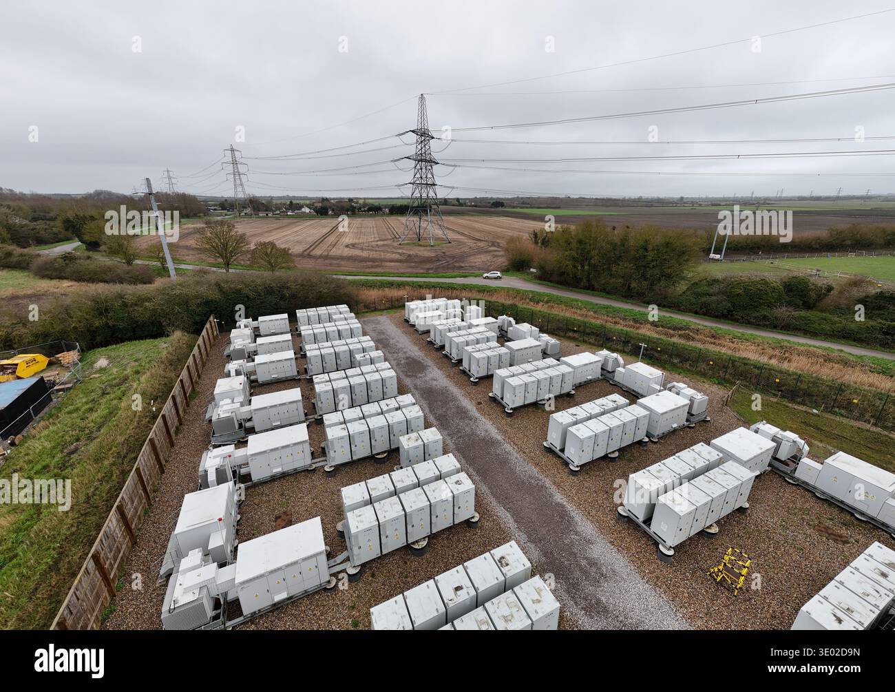 Aus der Vogelperspektive Reihen von unberührten weißen Behältern, die den Erdtönen von Feldern und den Skelettformen elektrischer Pylonen gegenüberstehen, Burwell, U Stockfoto