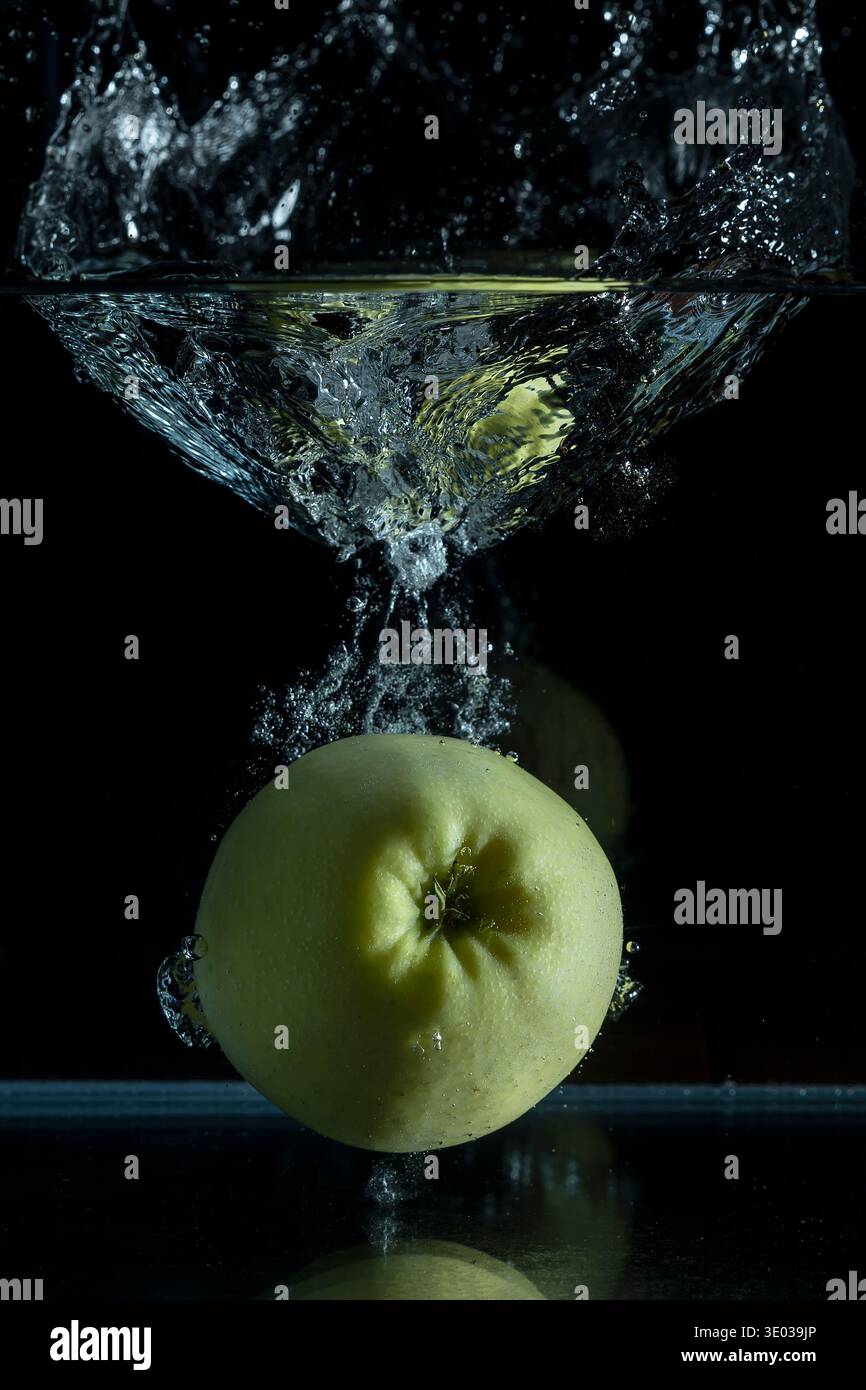 Ein grüner Apfel fällt in einen Glasbehälter, wodurch ein großer Spritzer entsteht Stockfoto