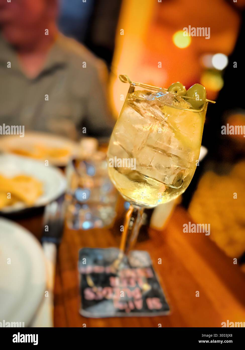 Nahaufnahme eines erfrischenden Cocktails garniert mit grünen Oliven auf einem Stock, der in einer schwach beleuchteten Bar oder im Restaurant serviert wird Stockfoto