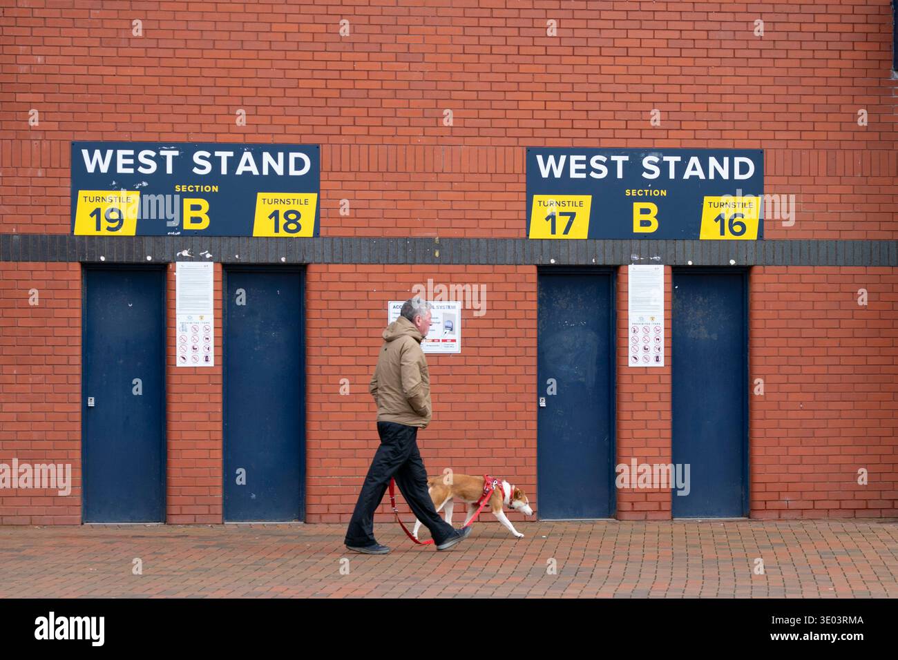 Mann geht mit Hund vorbei an Drehkreuzen im Hampden Park, dem National Stadium, Glasgow, Schottland, Großbritannien Stockfoto