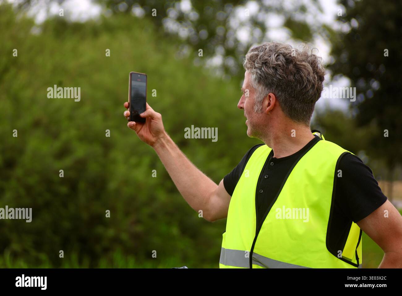 Seitenansicht eines männlichen Radfahrers mit reflektierender Sicherheitsweste mit Smartphone während einer Radtour auf dem Land. Stockfoto