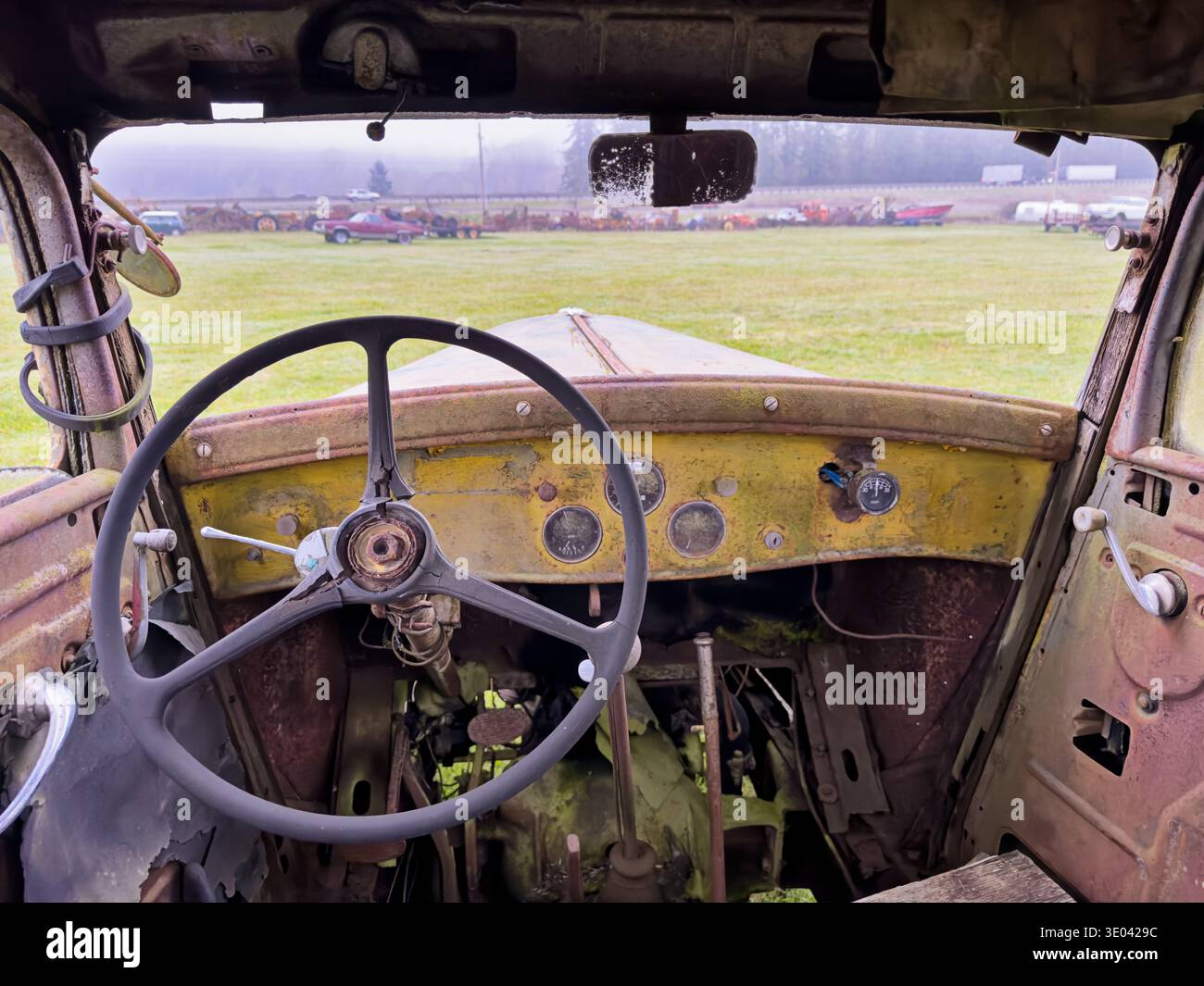 Eine Nahaufnahme des Lenkrads und des Armaturenbretts eines alten, rostenden Lkws mit Blick durch die Windschutzscheibe auf eine Reihe von gefallenen Fahrzeugen in der Notaufnahme Stockfoto