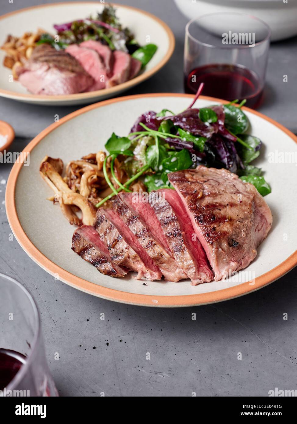 Zartes Steak in Scheiben auf einem Teller mit grünem Salat und Pilzen. Ein Glas Wein steht in der Nähe. Diese Mahlzeit eignet sich für eine proteinreiche Diät und Stockfoto