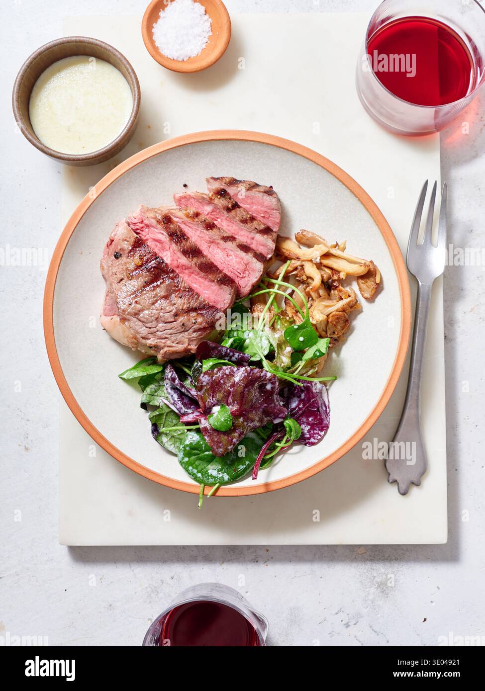 Gekochte Chuck zarte Steakscheiben stehen auf einem Teller neben einem frischen Salat und Pilzen. Zwei Gläser Rotwein stehen auf dem Tisch, was ein einfaches Dinner schafft Stockfoto