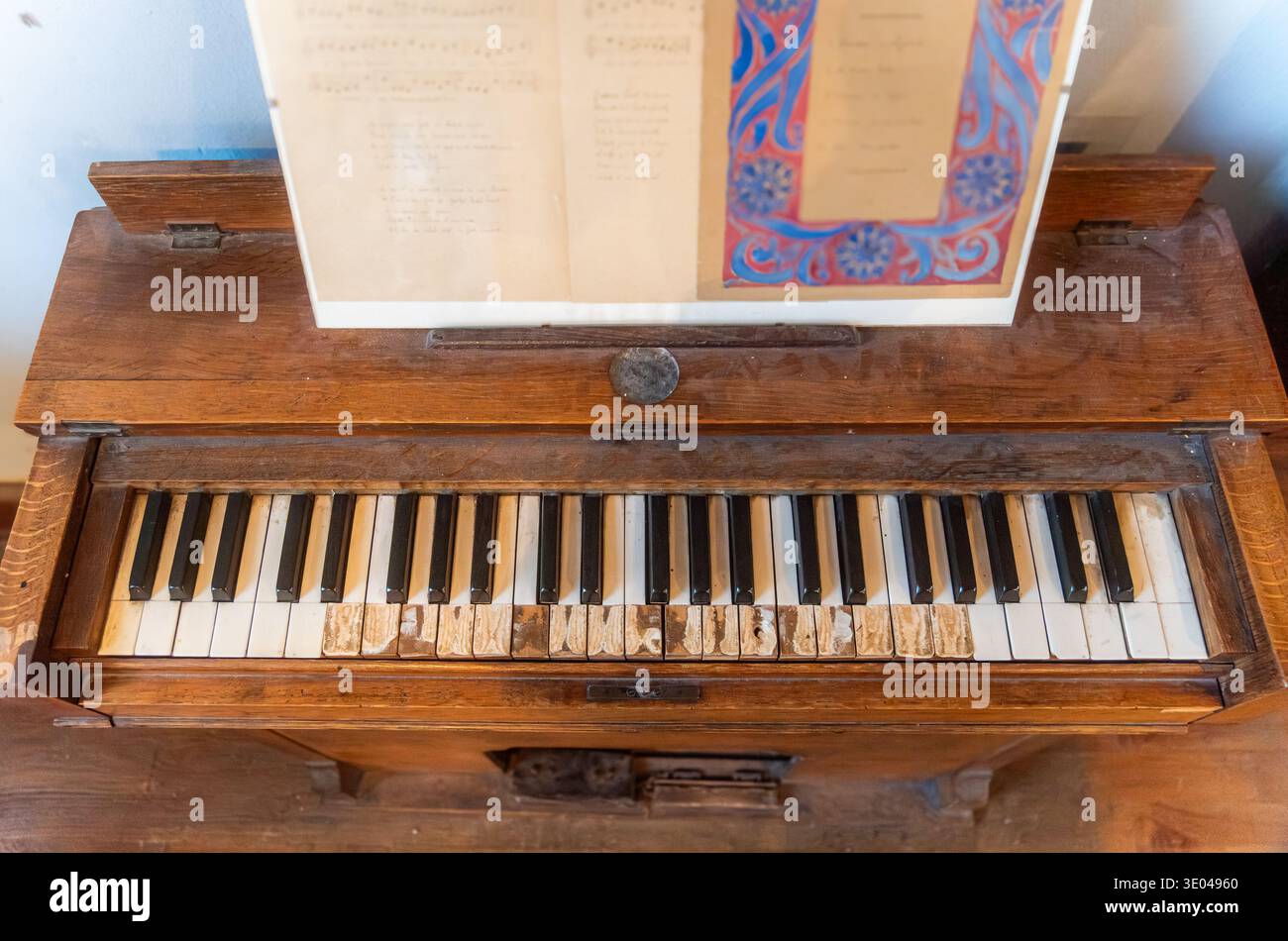 Ein Vintage-Holzpiano mit abgenutzten Tasten zeigt den Verlauf der Zeit. Die Notenblätter liegen auf dem Stand und erinnern an Nostalgie und das Wesen der klassischen Musik. Stockfoto