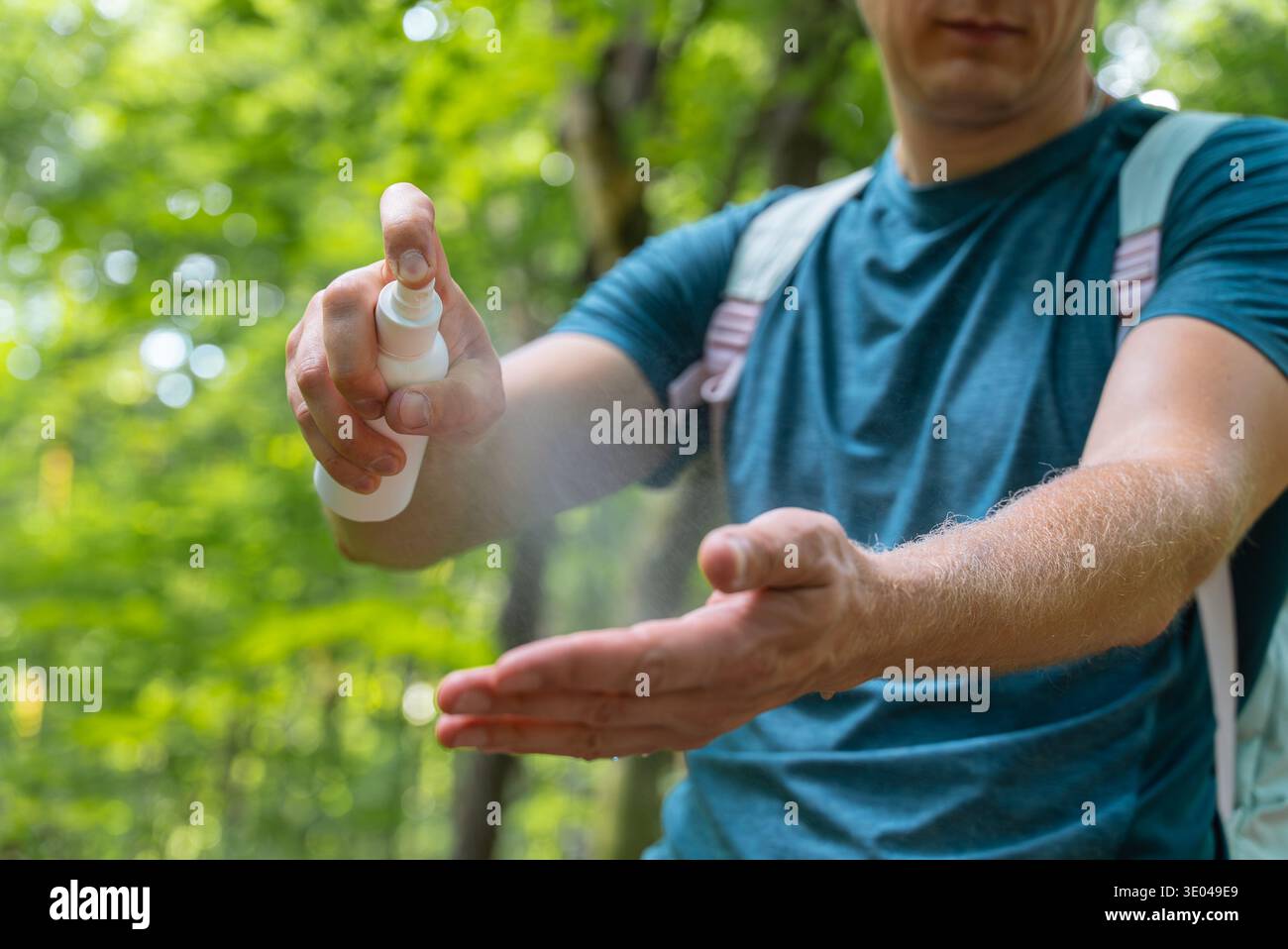 Mann, der Insektenschutzmittel auf die Haut mit üppigem Waldhintergrund aufträgt. Ziel ist es, den Schutz vor Insekten bei Wanderungen und Camping im Freien zu gewährleisten; Stockfoto
