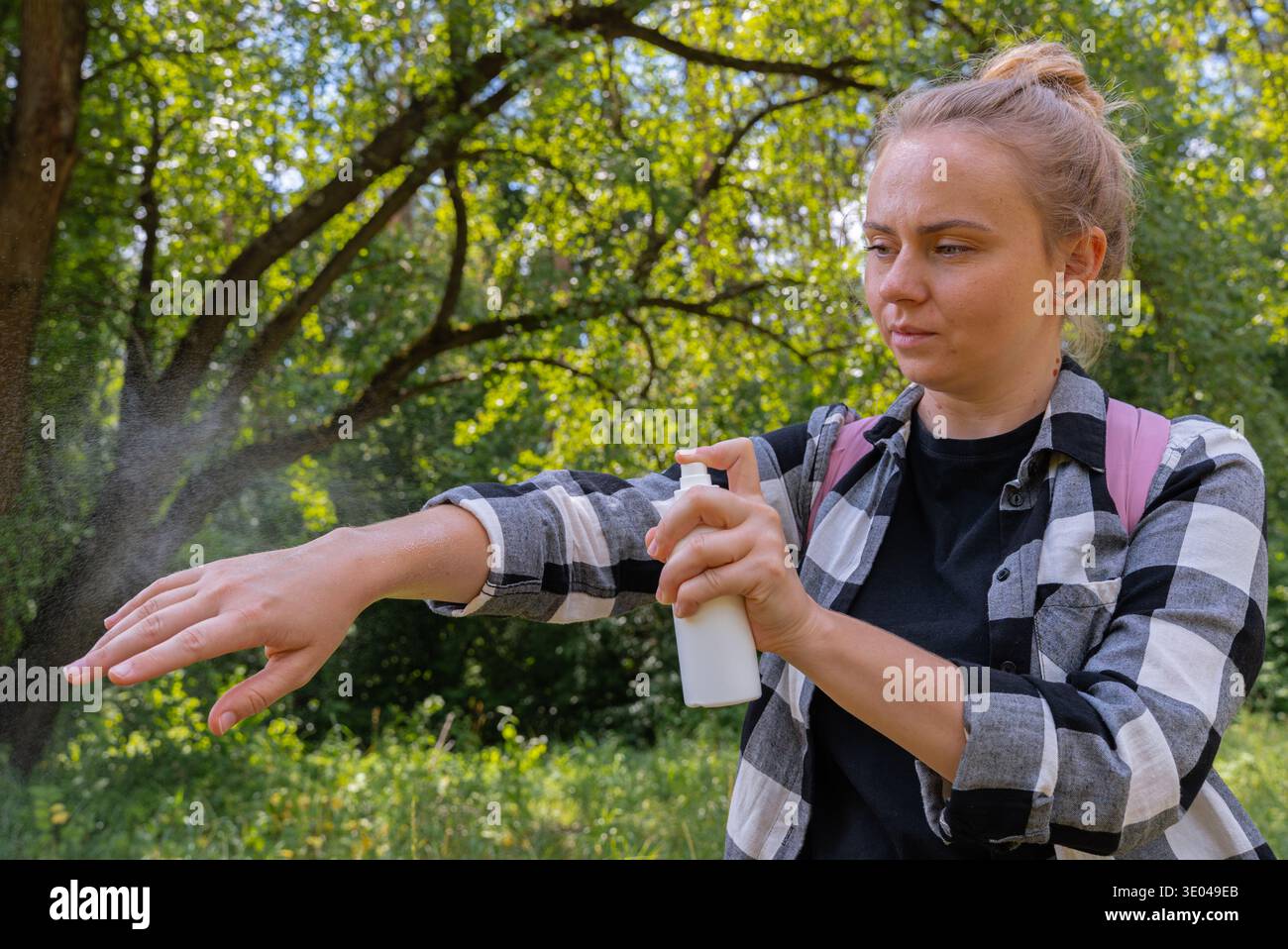 Eine Frau trägt Insektenspray auf ihren Arm auf, um die Haut vor Insekten zu schützen. In einer üppigen Umgebung im Freien, mit Schwerpunkt auf Körperpflege und o Stockfoto
