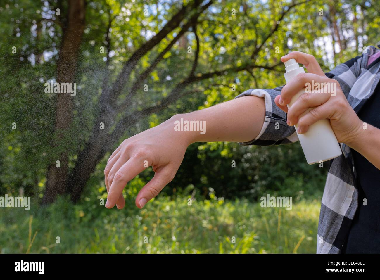 Eine Person sprüht Insektenschutzmittel im Freien auf ihren Arm, um einen effektiven Schutz der Haut vor Insekten hervorzuheben. Der üppige grüne Hintergrund betont einen Stockfoto