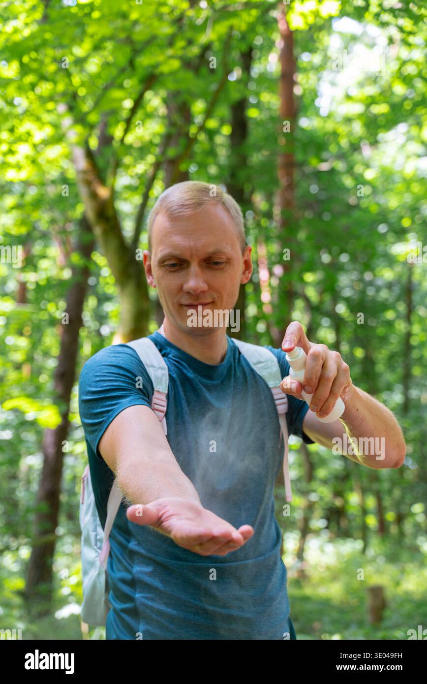 Ein Mann trägt Insektenspray auf seinen Arm auf, um effektiven Schutz vor Insekten zu bieten, während er Outdoor-Aktivitäten in einem üppigen, grünen Waldset genießt Stockfoto