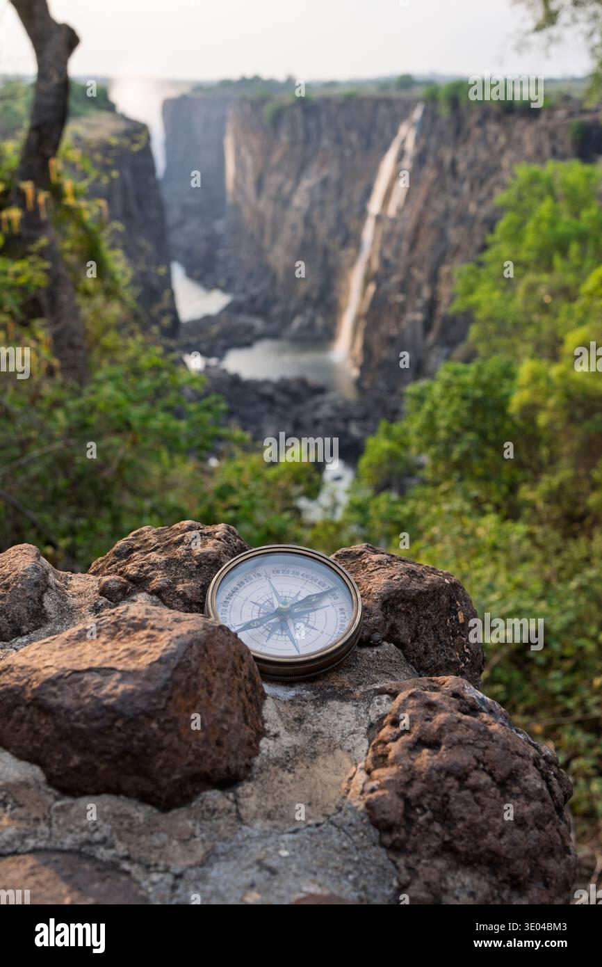 Ein malerischer Blick auf die Victoria Falls von der sambischen Seite, mit einem klassischen Kompass auf Felsen, symbolisiert Abenteuer und Entdeckungen in The Hear Stockfoto