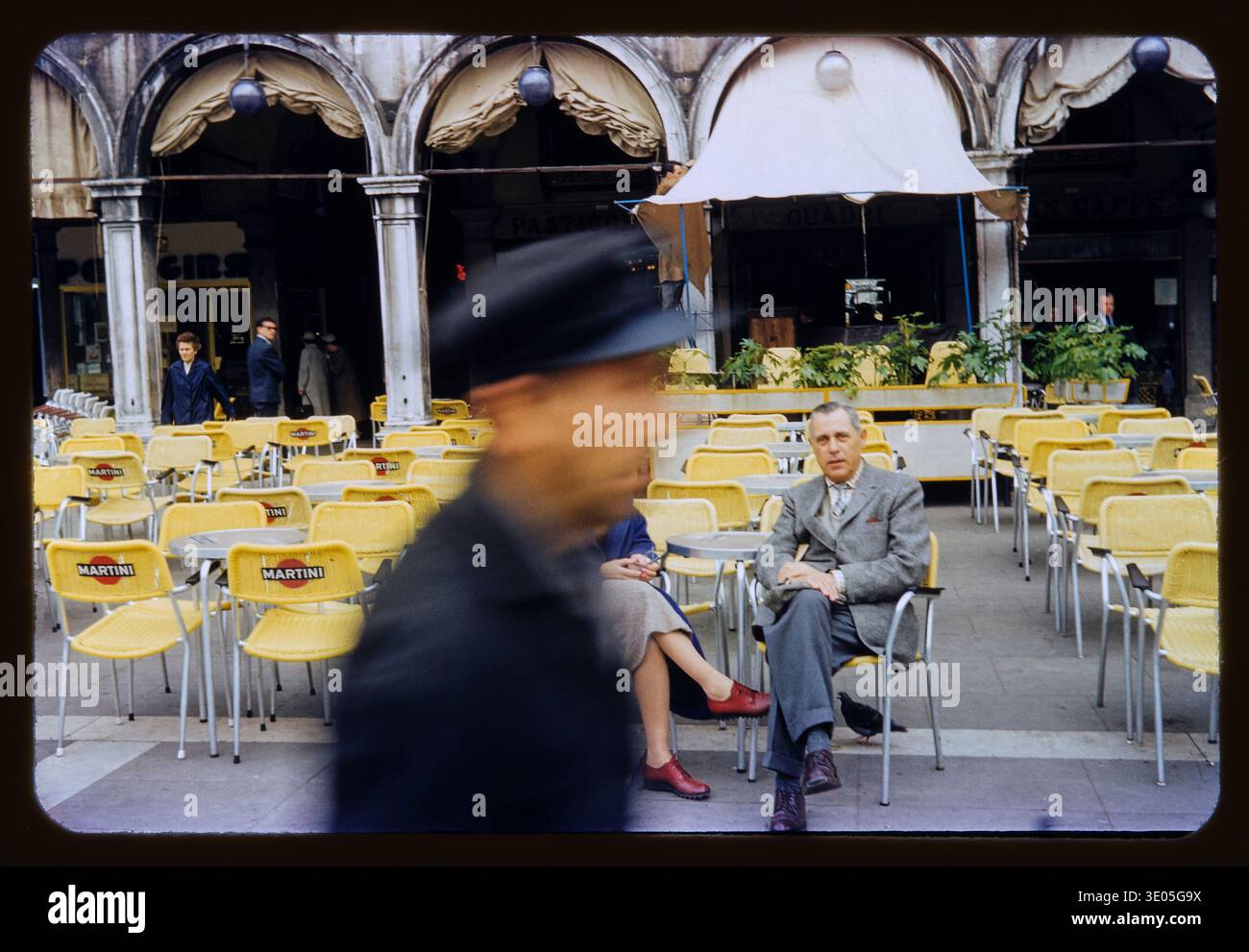 Ein amerikanisches Paar, Touristen, sitzt auf der Piazza San Marco in Venedig, Italien. Sie werden von einem vorbeiziehenden Mann fotografiert. Diese Folie, Kodachrome, wurde von einem amerikanischen Paar auf einer Reise nach Europa im Jahr 1959 aufgenommen. Die Farbe auf dem Foto ist lebendig, fast handgetönt, bemalt. Stockfoto