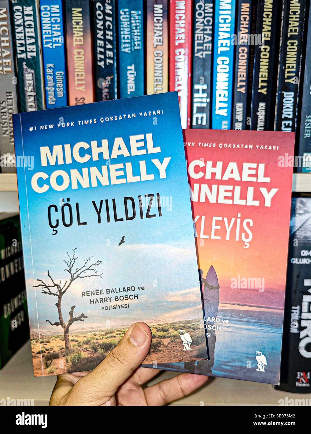 Hand hält türkische Ausgaben von Michael Connellys Romanen Harry Bosch und Renee Ballard vor einem verschwommenen Regalhintergrund. Stockfoto