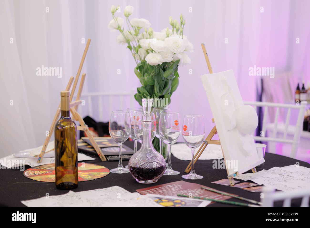Auf dem Jerewan Wine Days Festival präsentieren sie eine elegante Kunst- und Weingestaltung mit Staffeleien, Gläsern, Blumen und einer Karaffe in einem kreativen Festivalraum. Stockfoto
