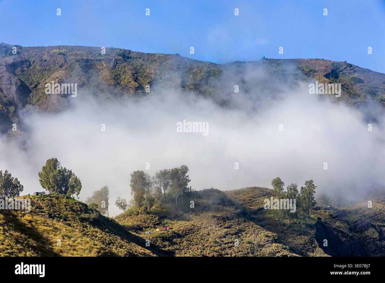 Dramatische Bergtallandschaft, die teilweise von dickem Nebel unter einem klaren blauen Himmel verdeckt wird Stockfoto