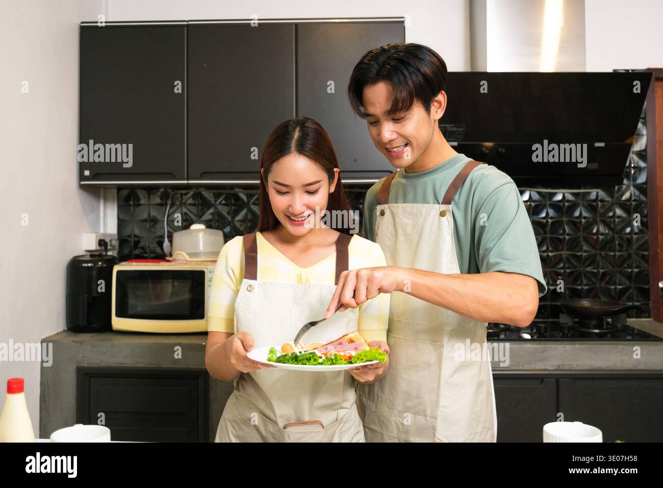 Asiatisches junges Paar, das in der Küche zu Hause kocht Stockfoto
