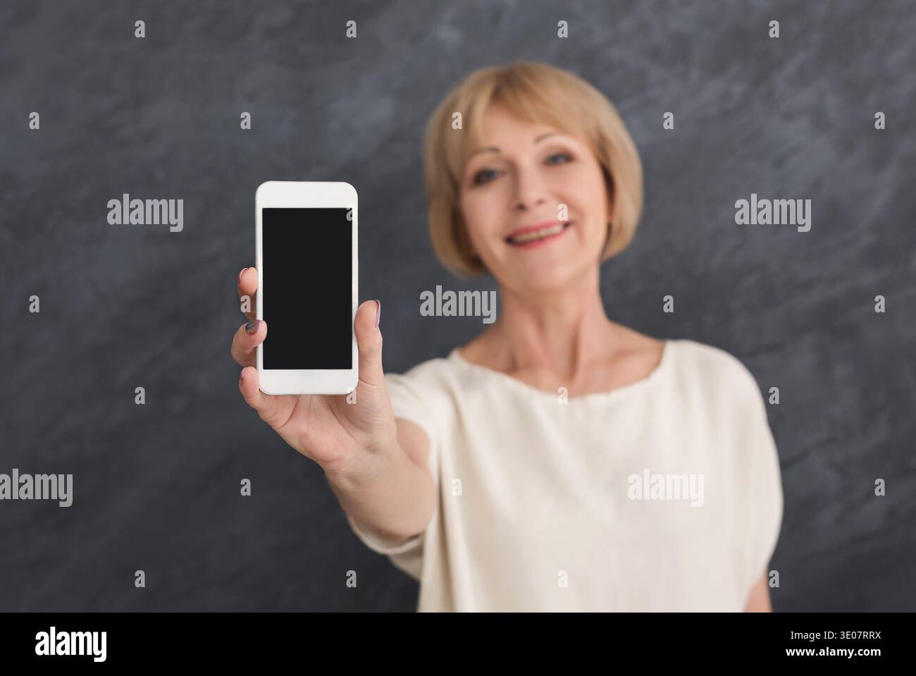 Lächelnde reife Frau, die ein Smartphone mit leerem Bildschirm hält Stockfoto
