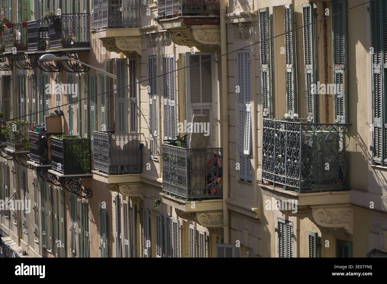 Wohnfassade mit kunstvollen schmiedeeisernen Balkonen und geschlossenen hellblauen Lamellen an der Außenfassade des Gebäudes in Nizza, Frankreich. Stockfoto