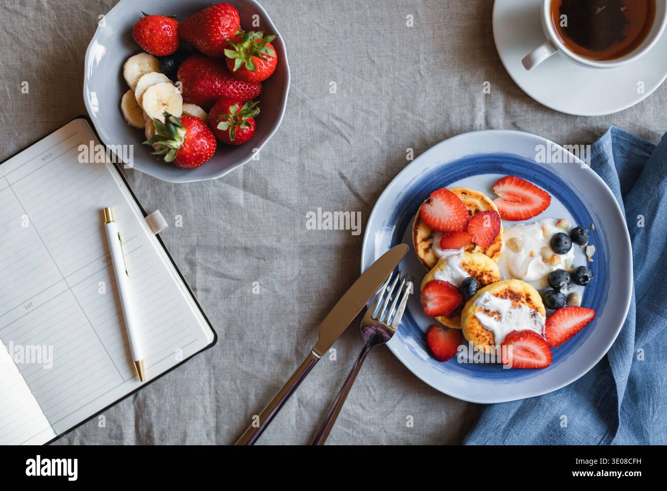 Blick von oben auf hausgemachte Keto Cottage Käse Pfannkuchen mit frischen Erdbeeren und Heidelbeeren, eine Schüssel Erdbeeren und eine Tasse Tee auf einem Tisch Stockfoto