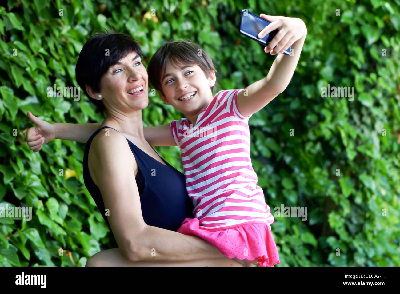 Liebevolle Familie, die im Sommer fröhliche Momente mit Selfie in lebendiger Umgebung teilt Stockfoto