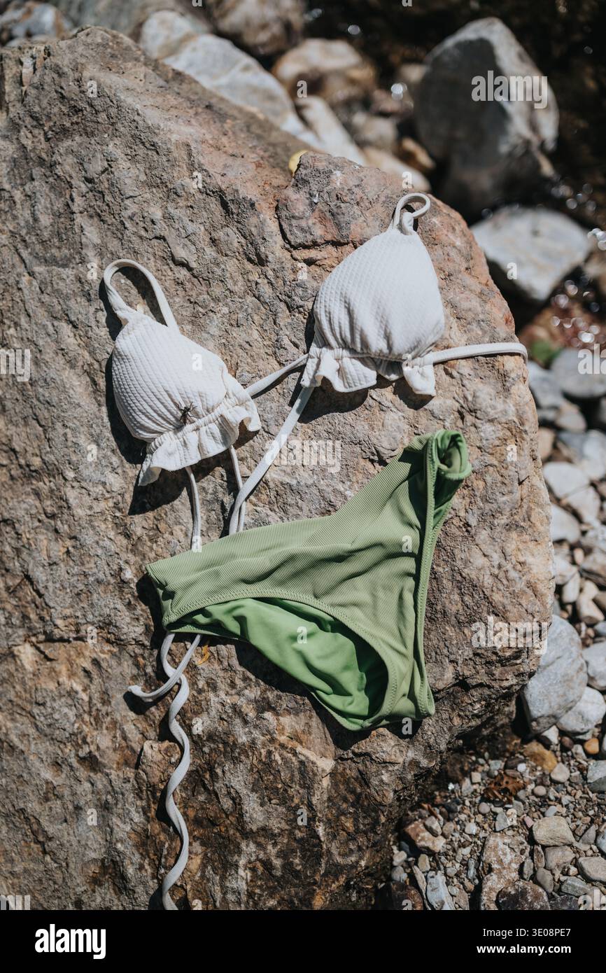 Weißes Bikinioberteil und grünes Bikiniunterteil auf Felsen am Flussufer Stockfoto