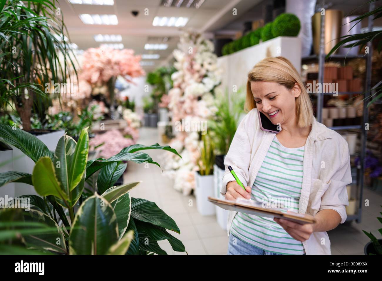 Der Blumenhändler macht sich Notizen, während er in einem Blumenladen telefoniert Stockfoto