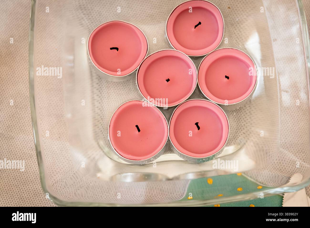 Ein Blick von oben auf sechs rosafarbene Teelichterkerzen, die in einer klaren Glasschale angeordnet sind. Stockfoto