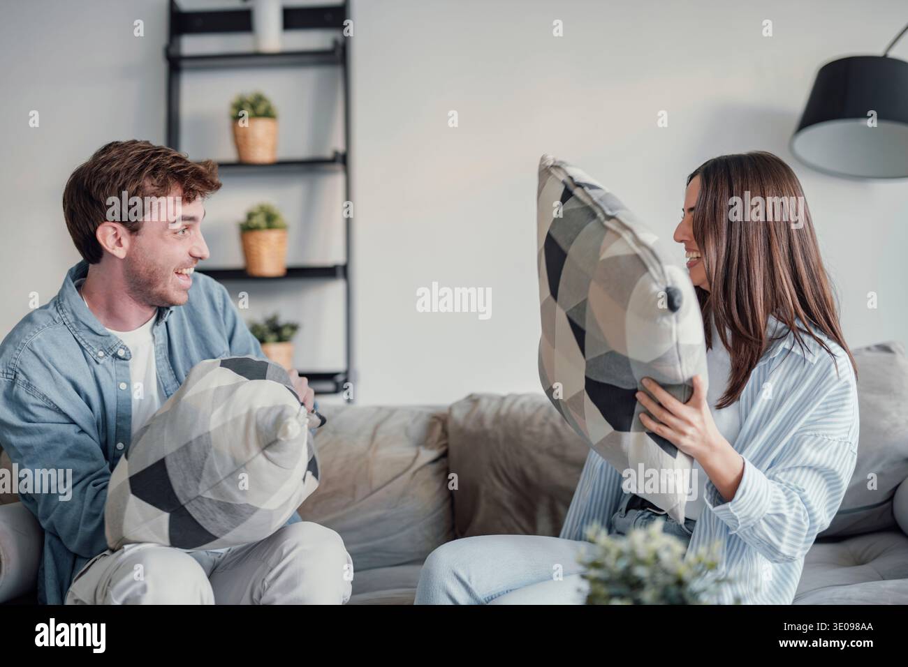 Fröhliches vielseitiges verheiratetes Paar, das zu Hause auf dem Sofa im Wohnzimmer sitzt. Millennials ziemlich gemischte Rasse Frau und kaukasischer Ehemann haben lustige Spielchen Stockfoto