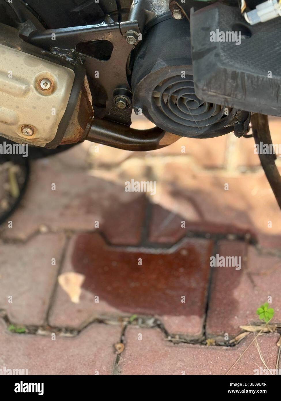 Motorradöl auf befestigtem Boden, was mechanische Wartungsprobleme hervorhebt. Mobiles Foto Stockfoto