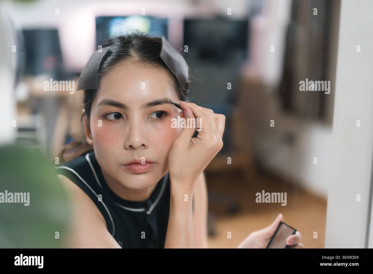 Nahaufnahme Porträt einer attraktiven asiatischen Frau, die sich bereit macht, Gesichtskosmetik aufträgt, Augenbrauen formt, Augenbrauen, Augenlinker vor dem Spiegel Stockfoto