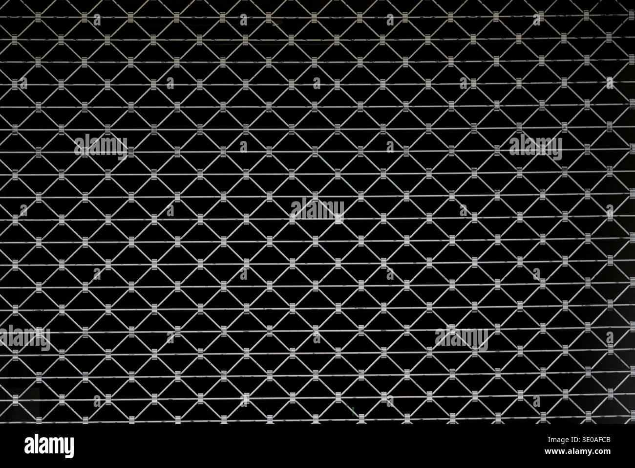 Moderne architektonische Details. Kontrastreiche geometrische Untersuchung des Sicherheitsgitters aus schwarzem Metall, wiederholtes Rautenmuster vor dunklem Hintergrund Stockfoto