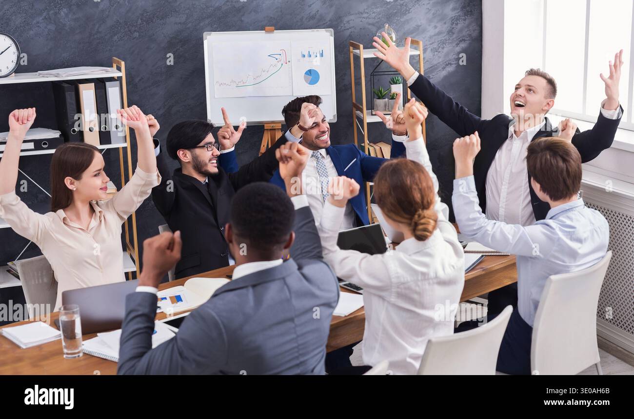 Fröhliche junge Leute, die aufgeregt im Büro sitzen Stockfoto