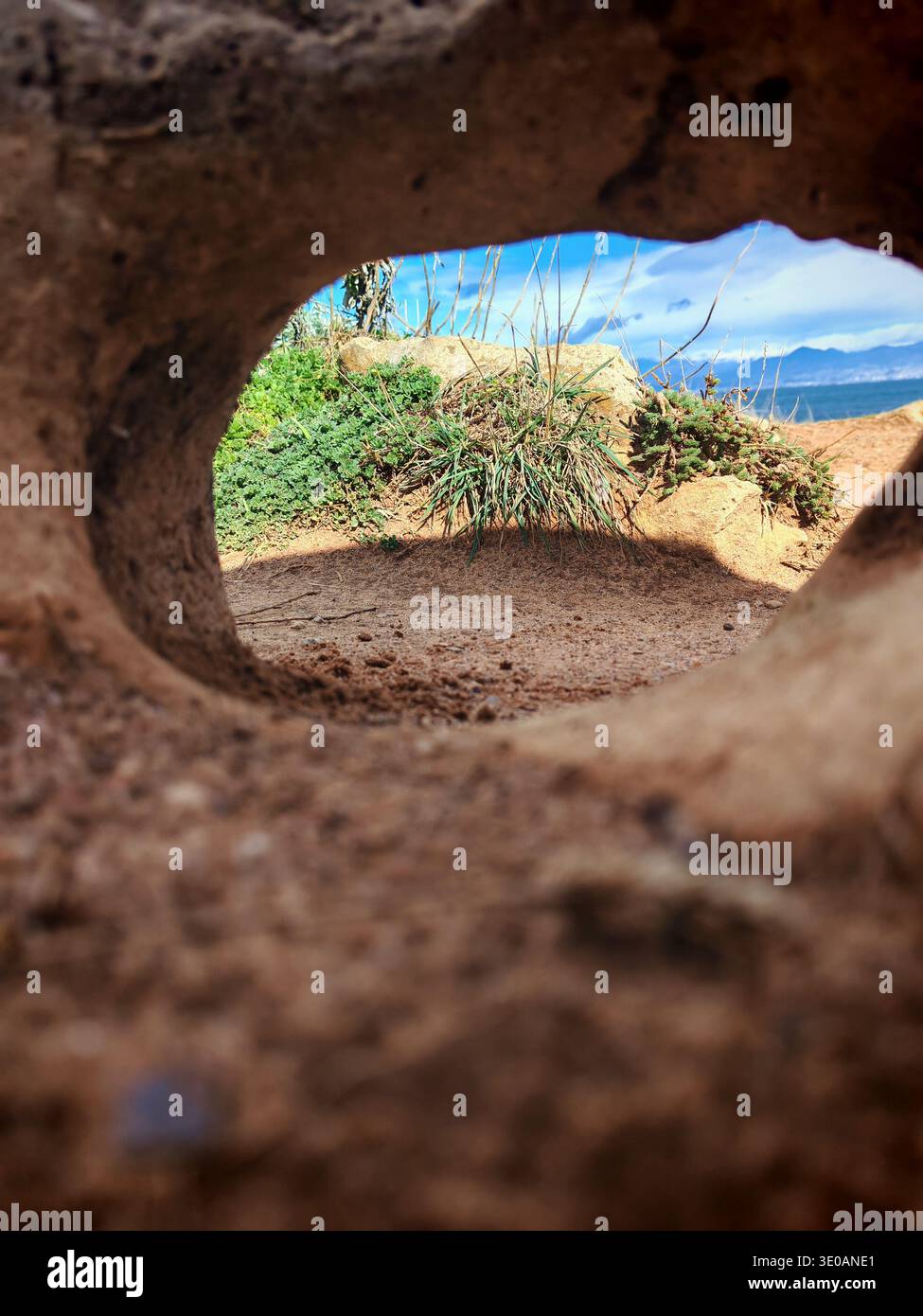 Viwe von Meer, Bergen und Gras ist durch das Loch in Stein am Strand in Frankreich Stockfoto
