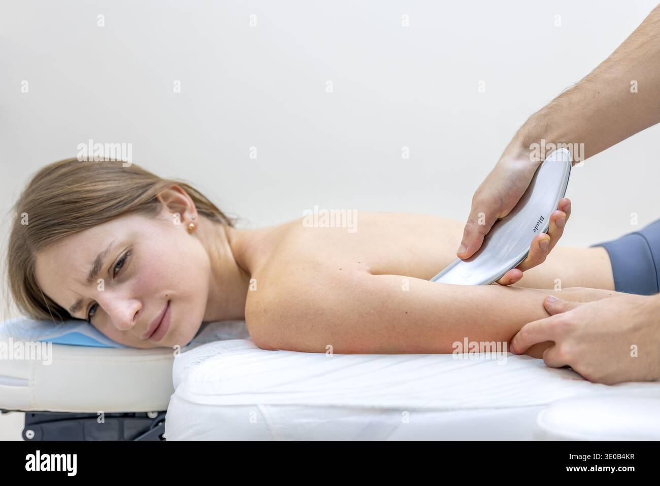 Der Reha-Arzt führt IASTM-Gua-Sha-Werkzeugarbeiten am Arm des Patienten durch. Werkzeugtherapie. Stockfoto