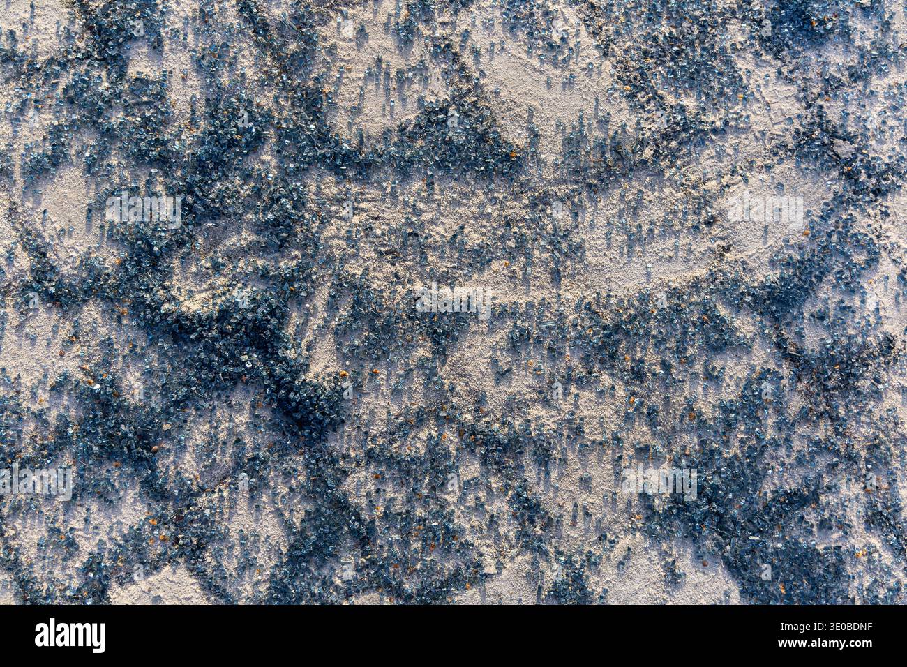 Blaue Kristallstruktur auf rauer Oberfläche. Abstrakte Nahaufnahme von verstreuten blauen Kristallen auf einem hellen, strukturierten Hintergrund, wodurch ein funkelndes Mineral entsteht Stockfoto