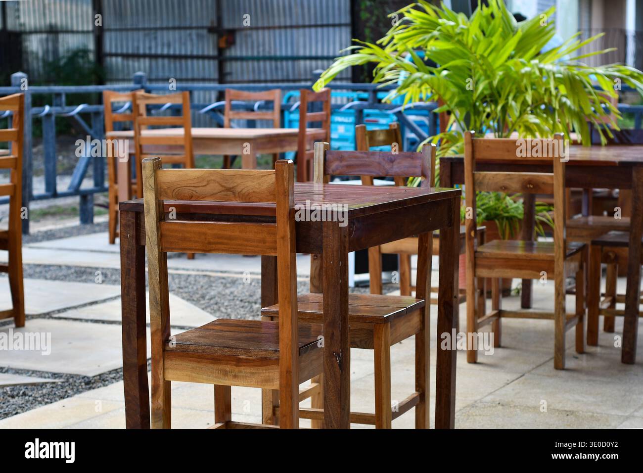 Ein einladender Sitzbereich im Freien mit polierten Holztischen und Stühlen auf einer gepflegten Terrasse aus Stein. Ein lebhaftes, grünes tropisches Pflanzenbild Stockfoto