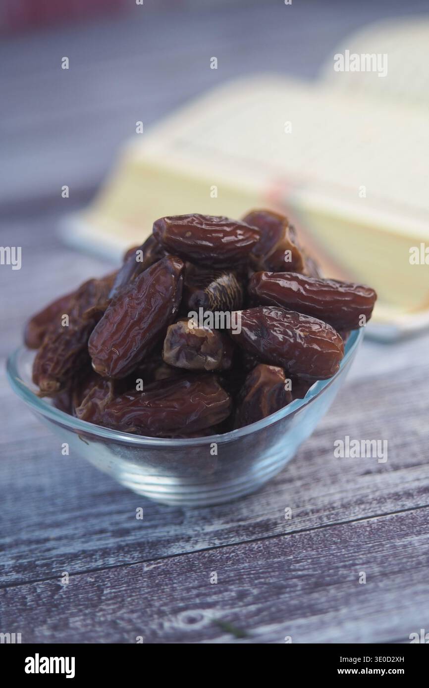 Eine Schüssel Datteln auf einem Holztisch mit einem Buch im Hintergrund Stockfoto