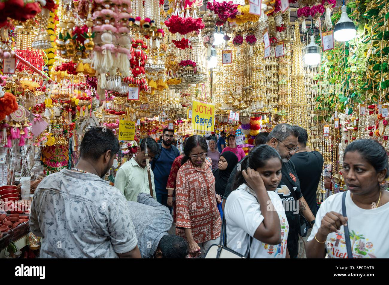 03.10.2025, Singapur, Singapur, - Menschen laufen unter bunten Blumengirlanden in Little India, die für hinduistische Gottesdienste und -Dienste genutzt werden Stockfoto