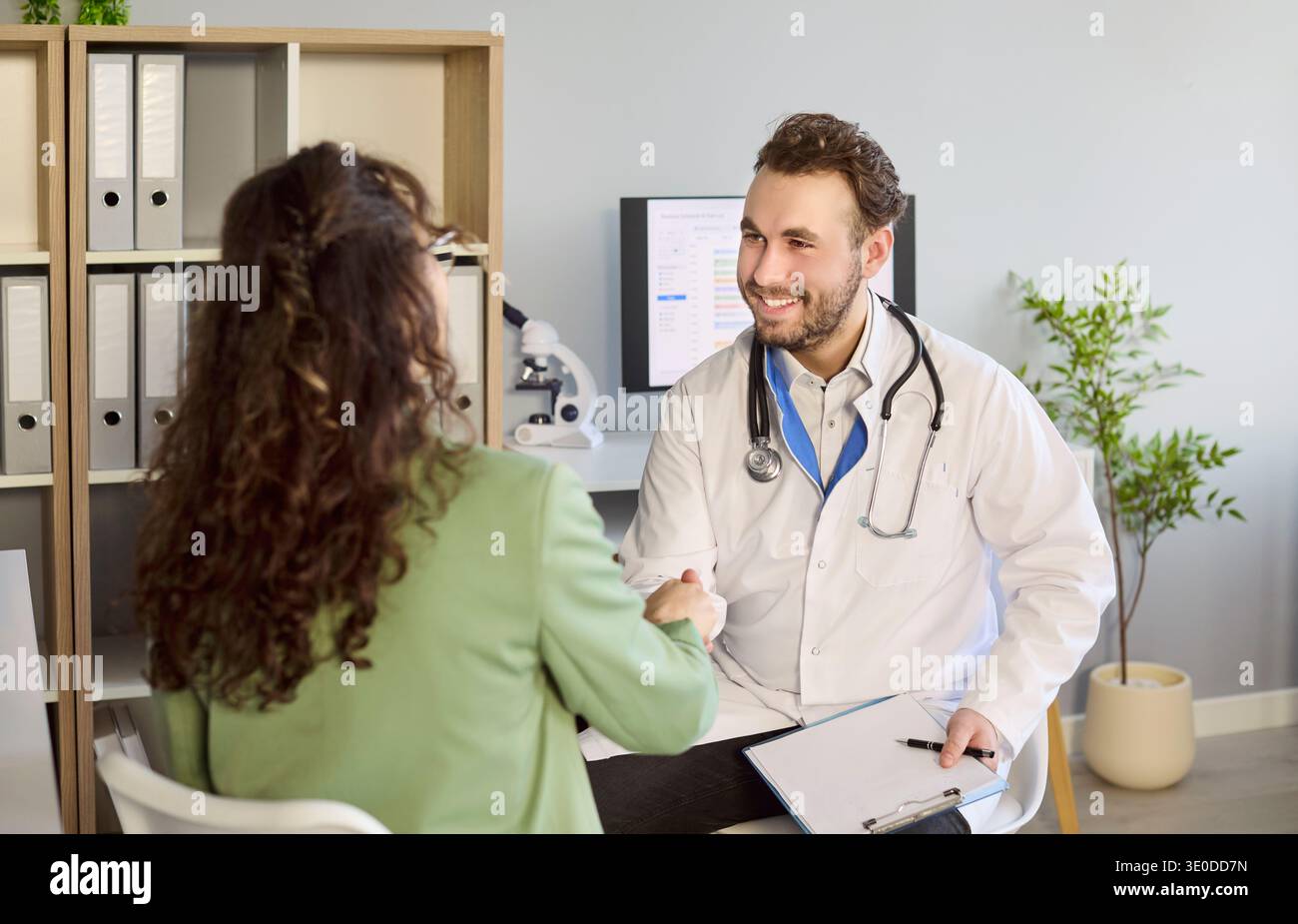 Lächelnder Arzt grüßt den Patienten mit Handschlag während der Sprechstunde in der Klinik Stockfoto