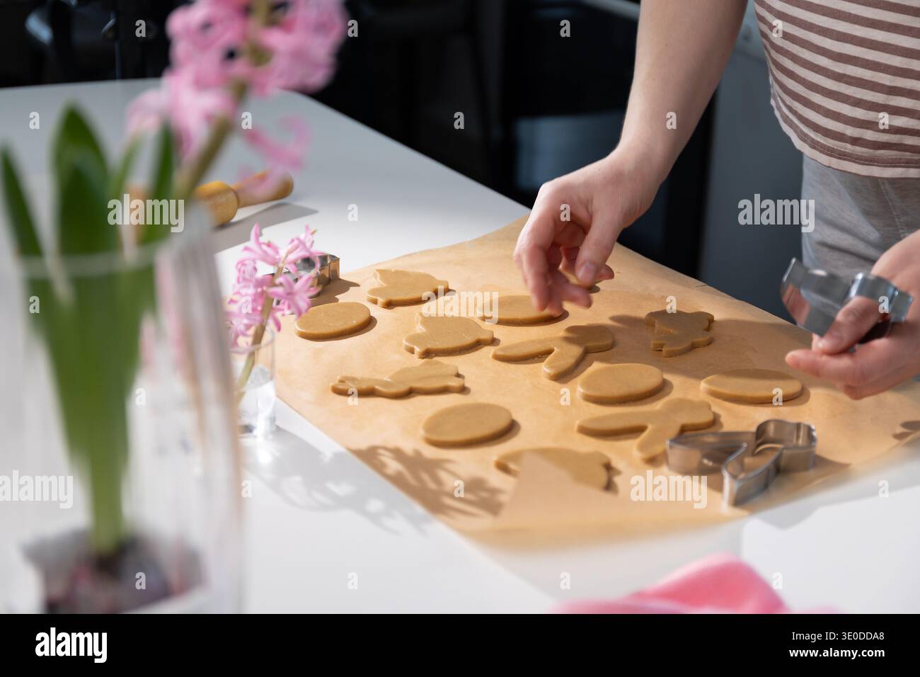 Hände Formen Lebkuchenkekse in verschiedenen Ostermotiven auf einer Arbeitsplatte in einer gemütlichen Küche. Familienmitglieder treffen sich, um sich auf die Feiertage und Traditionen vorzubereiten. Stockfoto
