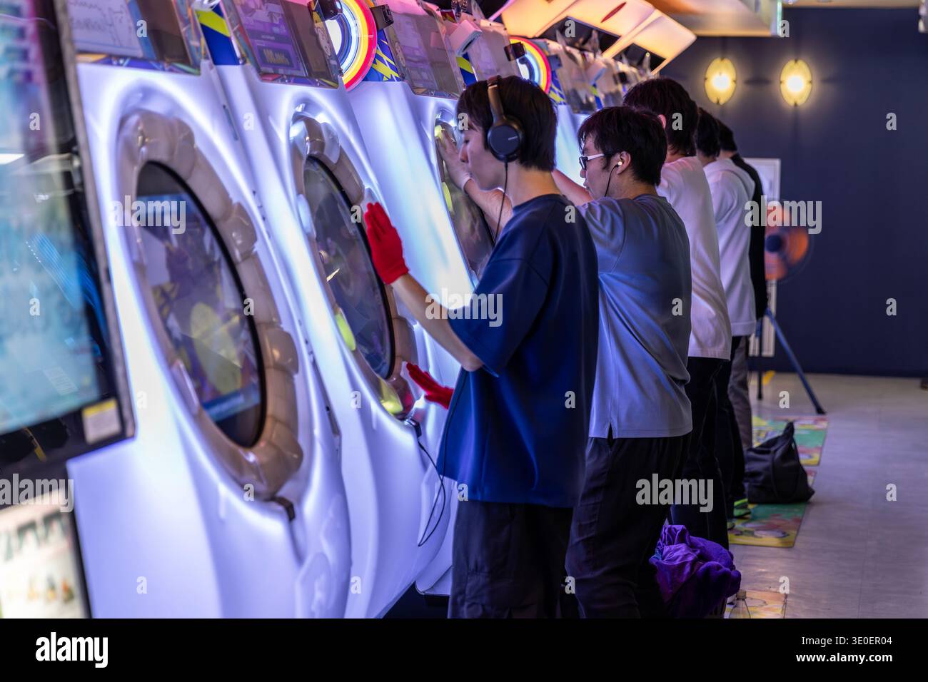 Junge Männer spielen leidenschaftlich Maimai-Spielautomaten in einem Unterhaltungszentrum Stockfoto