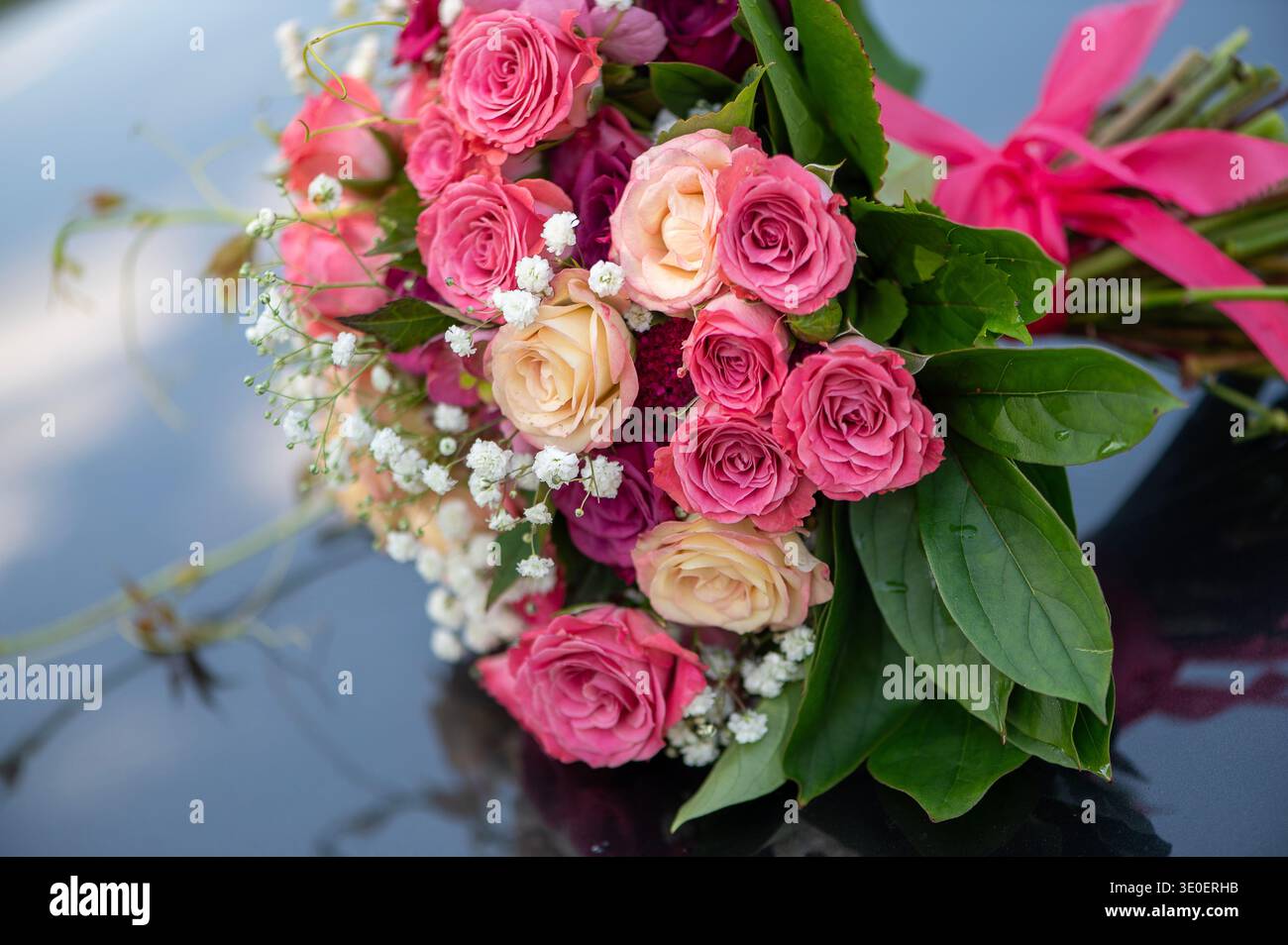 Eleganter Brautstrauß in Rosa und Creme-Rose auf einer glänzenden reflektierenden Oberfläche, die eine romantische und luxuriöse Hochzeitsstillen-Komposition schafft. Stockfoto