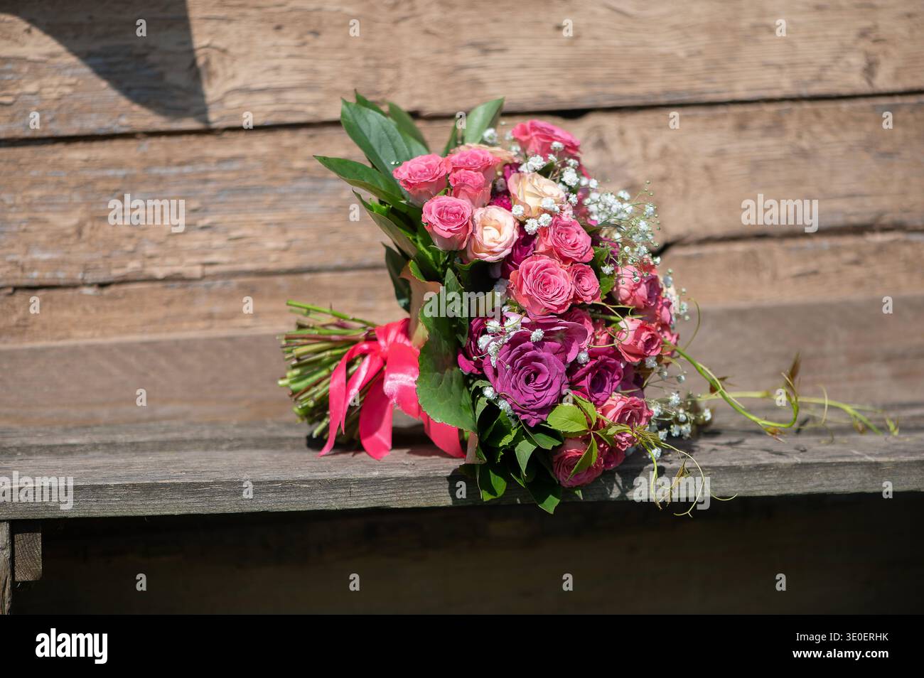 Rosa und cremefarbene Rosenstrauß auf einer rustikalen Holzbank, die natürliche Texturen mit elegantem Blumendesign verbindet. Stockfoto
