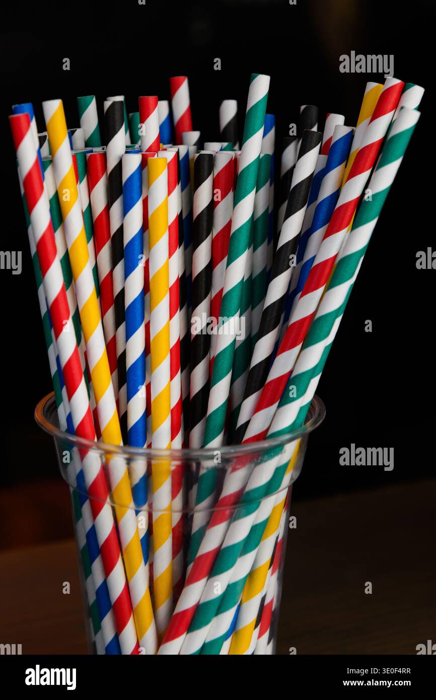 Ein klarer Glasbecher mit mehrfarbigen Trinkhalmen aus Papier und farbenfrohem Spiraldesign. Stockfoto
