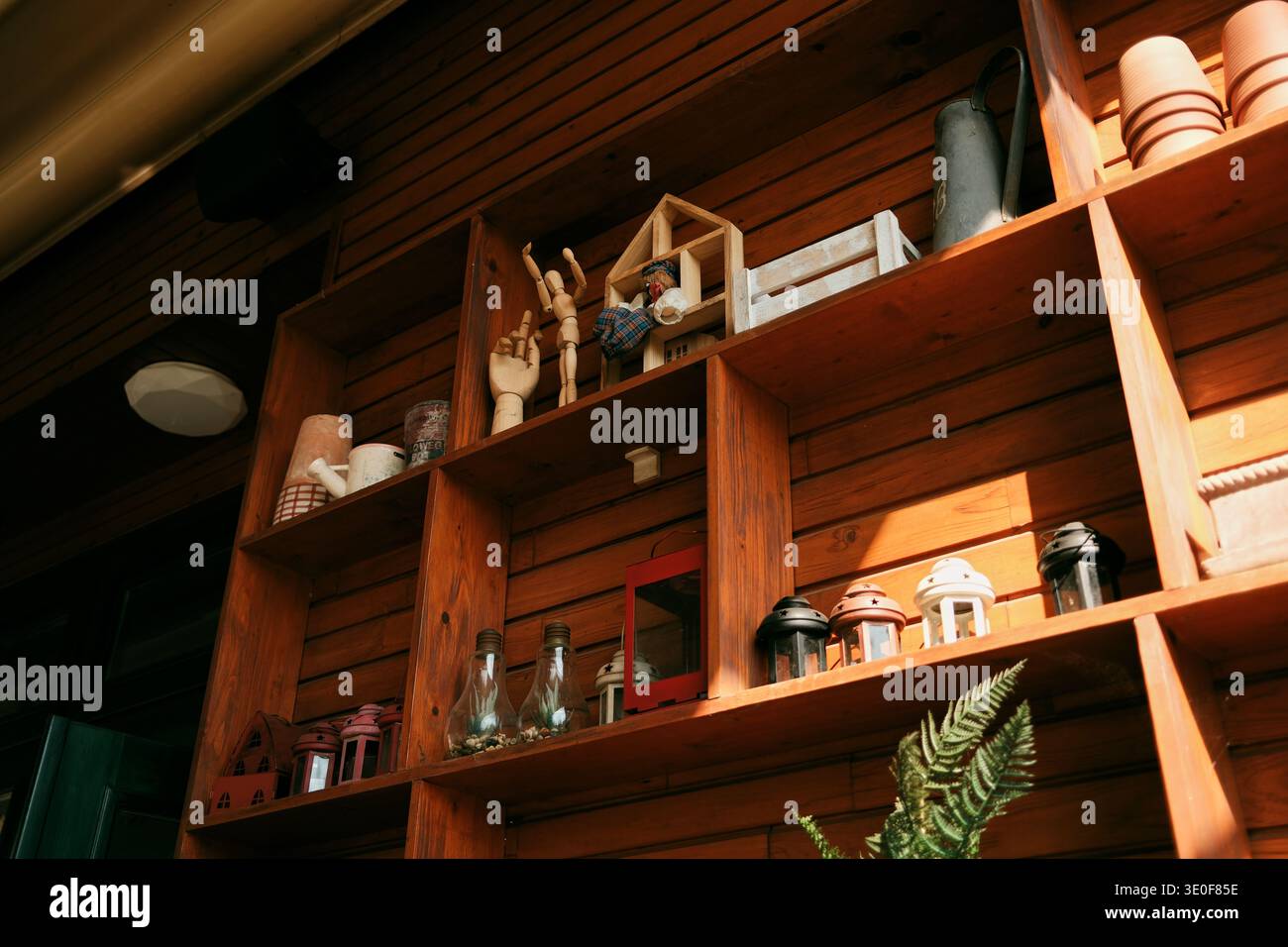 Holzregale mit dekorativen Gegenständen und Pflanzen in einem gemütlichen rustikalen Innenraum. Natürliche Texturen und warmes Sonnenlicht schaffen ein behagliches Zuhause Stockfoto